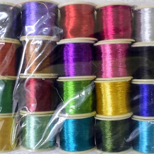 Può includere: Un pacchetto di colorate bobine di filo metallizzato. Le bobine sono disposte in file e colonne, con una varietà di colori tra cui argento, oro, rosso, rosa, viola, verde e blu. Il filo è avvolto strettamente su piccole bobine di plastica.