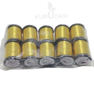 May include: A package of ten spools of gold-colored thread. Each spool is cylindrical with a black top and bottom. The thread is tightly wound, and the spools are packaged in clear plastic.