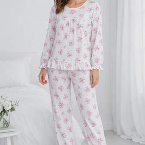 May include: White pajama set with a pink floral pattern. The long-sleeved top has a round neckline and ruffle detail. The pants have a matching floral print and ruffle cuffs. A comfortable sleepwear set.