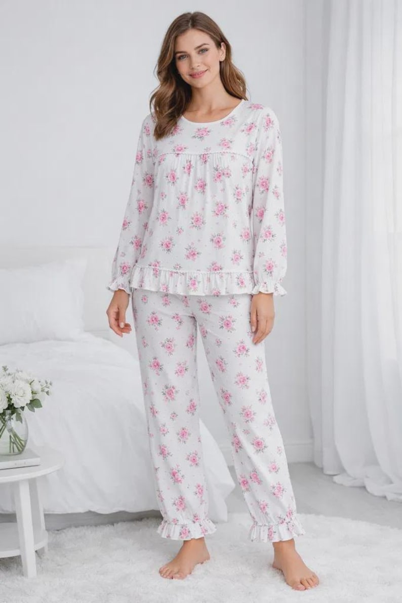 May include: White pajama set with a pink floral pattern. The long-sleeved top has a round neckline and ruffle detail. The pants have a matching floral print and ruffle cuffs. A comfortable sleepwear set.
