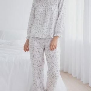 May include: A light-colored pajama set with a floral pattern. The long-sleeved top has a round neckline and ruffled cuffs. The matching pants have a relaxed fit and ruffled hems. The pajamas are made of a soft, lightweight fabric.