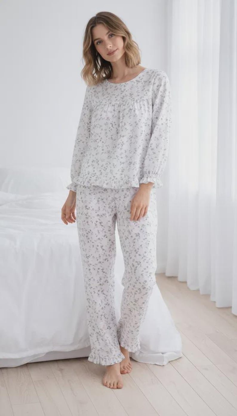 May include: A light-colored pajama set with a floral pattern. The long-sleeved top has a round neckline and ruffled cuffs. The matching pants have a relaxed fit and ruffled hems. The pajamas are made of a soft, lightweight fabric.