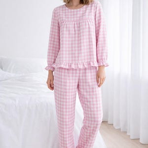 May include: Pink and white gingham pajama set. The long-sleeved top has a round neckline and ruffle trim at the cuffs and hem. The matching pants also have ruffle trim at the ankles. The pajamas are made of a soft, comfortable fabric.