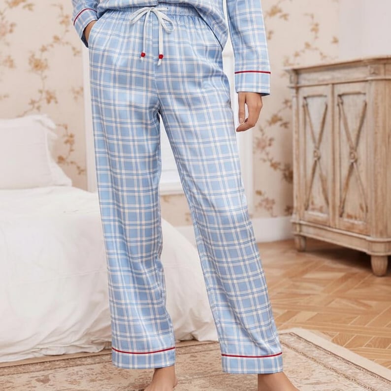 Op de afbeelding: Lichtblauwe geruite pyjamabroek met een trekkoord in de taille en rode bies. De broek maakt deel uit van een bijpassende set en is gemaakt van een zacht, zijdeachtig materiaal. Het ruitpatroon is een klassiek ontwerp.