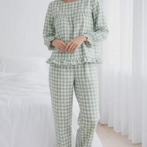 May include: A light green and white checkered pajama set. The long-sleeved top has a round neckline and ruffle trim at the cuffs and hem. The matching pants also have ruffle trim at the ankles. The pajamas are made of a soft, lightweight fabric.