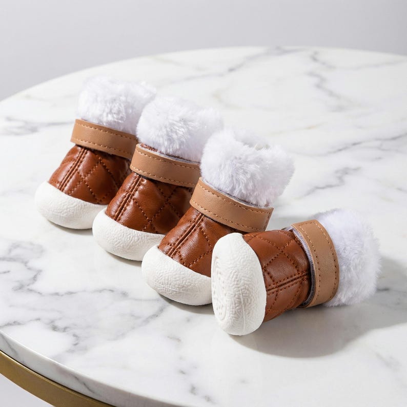 Op de afbeelding: Vier bruine hondenlaarzen met witte imitatiebontafwerking en witte zolen zijn gerangschikt op een marmeren oppervlak. De laarzen hebben een gewatteerd patroon en bruine bandjes. Deze accessoires zijn voor huisdieren.
