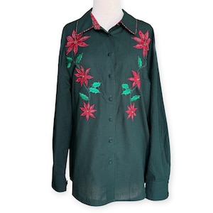 May include: A dark green button-down shirt featuring a fine black grid pattern and long sleeves. The front is decorated with embroidered red poinsettia flowers and green holly leaves. The collar interior displays a red and green plaid pattern.
