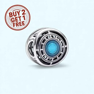 Może przedstawiać: Srebrny charms z geometrycznym wzorem i centralnym niebieskim akcentem. Charms ma okrągły kształt ze skomplikowanymi wzorami i widocznym słowem "Pandora". Czerwony okrągły grafika z tekstem "BUY 2 GET 1 FREE" znajduje się w lewym górnym rogu.