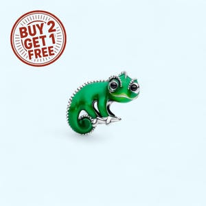 May include: A green chameleon charm with black eyes and silver accents. The charm has a detailed, textured design and is set against a light blue background. A red circular graphic with the text "BUY 2 GET 1 FREE" is in the upper left corner.