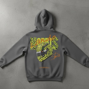May include: A gray hoodie featuring a graphic of a racing helmet with the name "Norris" in yellow and black. The hoodie has a hood and long sleeves. The back of the hoodie displays the helmet design and signature.
