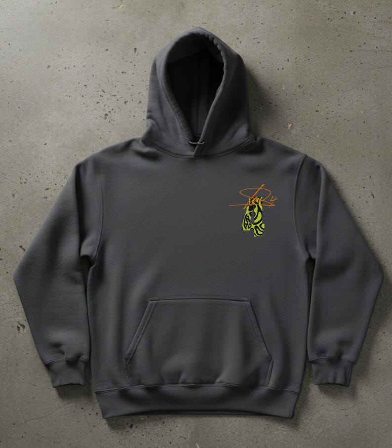 May include: A charcoal gray hoodie with a kangaroo pocket and a drawstring hood. The hoodie features a small, abstract design in yellow and orange on the upper left chest. The design appears to be a stylized signature or logo.