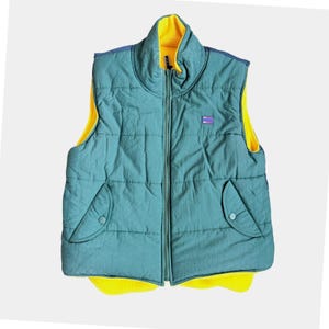May include: Teal puffer vest with a yellow interior and collar. The vest has a full zipper, two front pockets, and a small logo patch. The vest is a lightweight, quilted design.