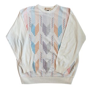 May include: Cream-colored sweater with a geometric pattern in shades of blue, orange, and purple. The sleeves and the lower part of the sweater are solid cream. The sweater has a crew neck and long sleeves.