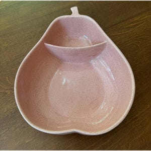 Puede incluir: Una fuente rosa en forma de pera con un pequeño compartimento adjunto. La fuente tiene una textura moteada y un acabado brillante. El diseño incluye un detalle de tallo en la parte superior. Esta fuente de estilo vintage es adecuada para servir aperitivos.