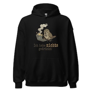 Könnte beinhalten: Schwarzer Kapuzenpullover mit einer Grafik eines Vogels und eines brennenden Laptops. Der deutsche Text "Ich habe nichts gedrückt!" ist in Gold gedruckt. Der Hoodie hat eine Kapuze und eine Vordertasche.