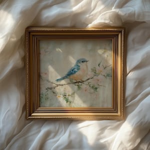 May include: A framed painting featuring a blue bird perched on a flowering branch. The artwork is set within a gold-colored frame. The bird has blue and orange plumage, and the flowers are a soft pink.