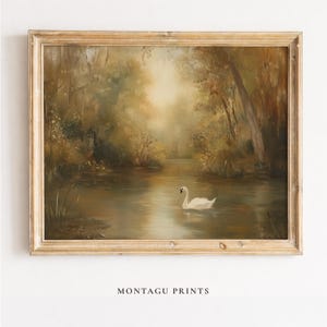 Pode incluir: Pintura a óleo de uma serena cena lacustre com um cisne branco flutuando na água. A obra de arte apresenta uma moldura de madeira dourada e folhagem exuberante e detalhada ao longo da margem da água. O texto "MONTAGU PRINTS" está na parte inferior.