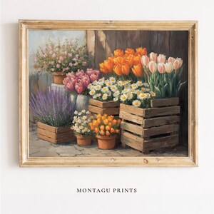 May include: A framed print featuring a floral arrangement. The artwork showcases various flowers, including tulips, daisies, and lavender, displayed in wooden crates and pots. The color palette includes orange, pink, white, and purple hues. The text "MONTAGU PRINTS" is at the bottom.