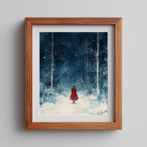 Op de afbeelding: Een ingelijste kunstdruk toont een persoon in een rode jas die door een besneeuwd bos loopt. Het kunstwerk maakt gebruik van een donkerblauw en wit kleurenpalet, met vallende sneeuw en hoge bomen. Het frame is van hout.