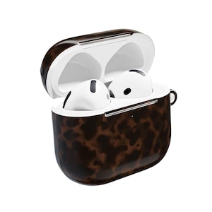 Puede incluir: Estuche abierto para AirPods con un patrón marrón y negro. En el interior, se ven dos auriculares blancos. La funda tiene un acabado brillante y un pequeño lazo. Los auriculares tienen detalles en negro.