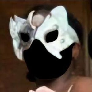 May include: A decorative mask with a split design, featuring a combination of white, gray, and black colors. The mask has eye openings and a black lower section. The image also includes a bouquet of pink and purple flowers.