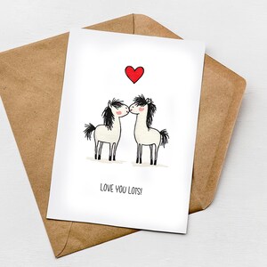 May include: A white card featuring two cartoon horses kissing beneath a red heart, with the text "LOVE YOU LOTS!". The card rests on a brown envelope. The design is simple and sweet, suitable for a romantic or affectionate message.