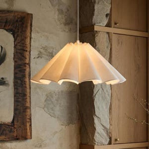 Può includere: Una sala da pranzo con un tavolo in legno e sedie nere. Una lampada a sospensione con paralume in carta è appesa sopra il tavolo. Una ciotola decorativa è sul tavolo. Le pareti sono in pietra e la stanza ha una palette di colori neutri.