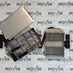 Puede incluir: Una vista aérea de instrumentos y bandejas quirúrgicas. La imagen presenta tres bandejas metálicas, una rectangular con perforaciones y dos bandejas rectangulares que contienen instrumentos quirúrgicos. El texto "MOVIN SURGICAL INDUSTRIES" es visible.