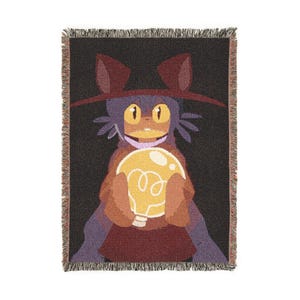 May include: A woven throw blanket featuring a cartoon character holding a glowing lightbulb. The character has a cat-like appearance with a hat and is set against a black background. The blanket has a fringed edge and is primarily brown, purple, and yellow.