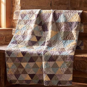 Könnte beinhalten: Eine Steppdecke mit einem sich wiederholenden geometrischen Muster aus Dreiecken in verschiedenen gedeckten Farben wie Staubblau, sanftem Gelb, Dunkelbraun und Lavendel. Die Stoffstücke zeigen diverse kleinteilige Blumen- und Karomuster mit sichtbaren Nähten.