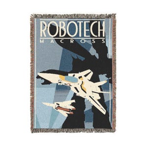 May include: Woven throw blanket featuring a design with the text "ROBOTECH MACROSS" and illustrations of fighter jets in flight. The blanket has a light blue background with a fringed edge. The jets are white, yellow, and blue.
