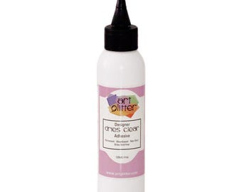 May include: A white bottle of "art glitter" designer dries clear adhesive with a black nozzle. The label is pink and white with the text "Designer dries clear Adhesive". The bottle contains 4 fl oz.