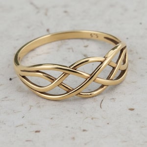 Puede incluir: Un anillo dorado con un diseño de nudo celta entrelazado. El anillo está hecho de metal brillante y pulido, con un patrón continuo y fluido. El anillo está sobre un fondo neutro. El diseño es un símbolo de eternidad.
