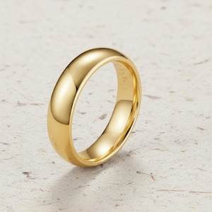 Puede incluir: Un anillo de oro pulido con una banda lisa y redondeada. El anillo tiene una superficie brillante y reflectante, sobre un fondo neutro. Este diseño clásico es adecuado para diversas ocasiones. La banda del anillo mide unos 0,3 cm de ancho.