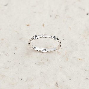 Könnte beinhalten: Ein silberner Ring mit einem sich wiederholenden Fischmuster. Der Ring besteht aus glänzendem Metall und weist eine Reihe stilisierter Fische um das Band auf. Der Ring ist innen mit "925" markiert.