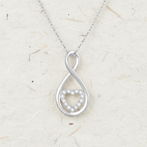 Puede incluir: Collar con colgante plateado con un diseño de símbolo de infinito y un corazón con pequeñas gemas transparentes en el centro. La cadena delicada crea un aspecto simple y elegante. Ideal para regalo.