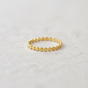 May include: A delicate gold ring featuring a repeating pattern of small, circular accents. The ring has a thin band and a polished finish, reflecting light. The design is simple and elegant, suitable for everyday wear. The ring is shown on a neutral background.