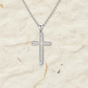 May include: A silver-colored pendant necklace featuring a cutout cross design. The cross hangs from a delicate chain, creating a simple yet elegant piece of jewelry. The pendant has rounded edges and a polished finish, reflecting light.