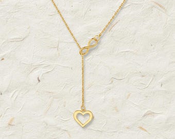 May include: A gold-colored necklace featuring an infinity symbol and a heart pendant. The necklace has a delicate chain and a Y-shaped design. The heart pendant is a hollow outline. The jewelry is displayed against a textured, off-white background.