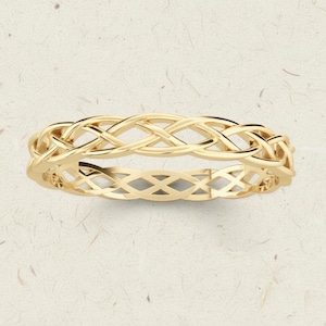 Könnte beinhalten: Ein goldfarbener Ring mit einem keltischen Knotenmuster. Der Ring hat ein ineinander verwobenes Muster, das ein durchgehendes, strukturiertes Band bildet. Das Design des Rings ist symmetrisch und scheint aus poliertem Metall zu bestehen.