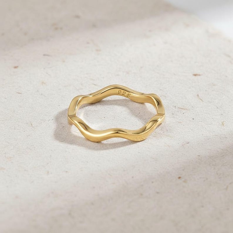 May include: A gold-colored ring with a wavy, organic design. The ring has a smooth, polished finish and the number "925" is stamped on the inside. The ring is set against a neutral background.