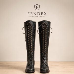 以下が含まれることがあります： ダークブラウンの靴紐と金属製のアイレットを備えた、前面フルレースアップデザインの黒い膝丈ブーツ。ブーツの上部には、文字Fが入った盾のロゴとFENDEX HANDMADEというテキストが配置されています。