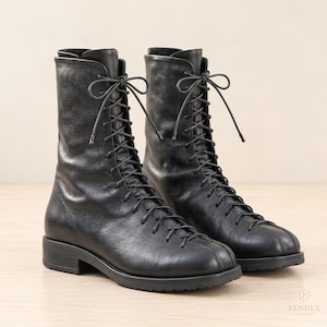 May include: A pair of black leather mid-calf boots featuring a lace-up front closure with thin black laces, a rounded toe, and a low block heel. The boots have a smooth texture and a vertical seam detail running along the center of the toe box.