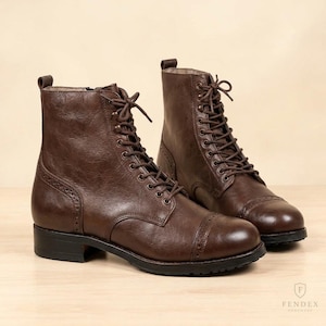 Puede incluir: Un par de botas con cordones de color marrón oscuro que presentan una puntera con detalles decorativos tipo brogue, cierre de cremallera lateral, una trabilla en el talón y una suela negra. Las botas tienen un acabado liso y cordones marrones.