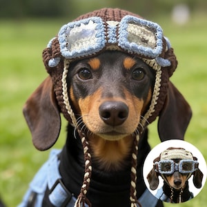May include: A dachshund dog wearing a brown and blue crocheted aviator hat with goggles. The dog has brown and black fur and is wearing a blue denim vest. The hat has a braided strap.