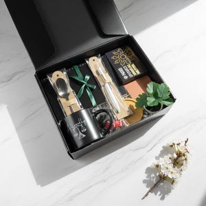 May include: A black gift box containing a mug, spoon, pen, notepad, and small plant. The mug features the word "Allegedly" and a scales of justice graphic. The box is open, displaying the contents, on a marble surface.