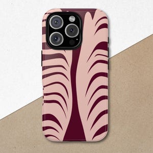 May include: A phone case with a pink and burgundy abstract design. The case features a repeating pattern of curved lines against a light pink background. The phone case has a black camera module.