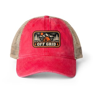 Op de afbeelding: Een rode baseballpet met een beige mesh achterkant en een rechthoekige patch aan de voorzijde. De patch heeft een zwarte achtergrond met een oranje zon, witte bergen, dennenbomen en een tent, met de tekst OFF GRID in witte letters.