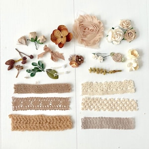 May include: An assortment of craft supplies, including fabric flowers in shades of cream, tan, and brown, along with various ribbons and lace trims. The items are arranged on a white surface, perfect for DIY projects and scrapbooking.