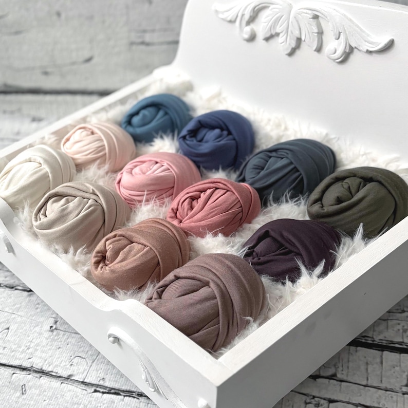 May include: A white decorative tray filled with rolled fabric in various colors, including beige, pink, blue, and green. The fabric is arranged on a bed of white faux fur. The tray has ornate carved details.